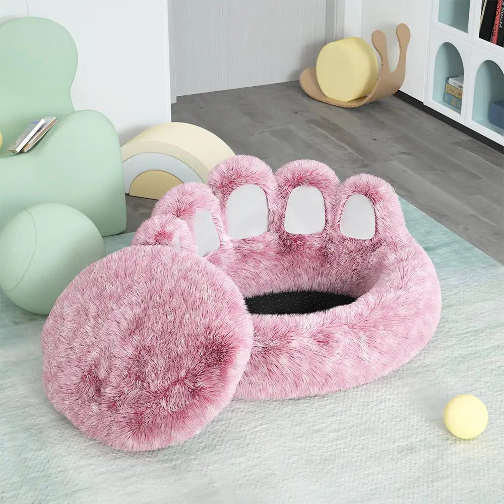 Pink paw-shaped pet bed on a light green rug with colorful chairs in the background.
