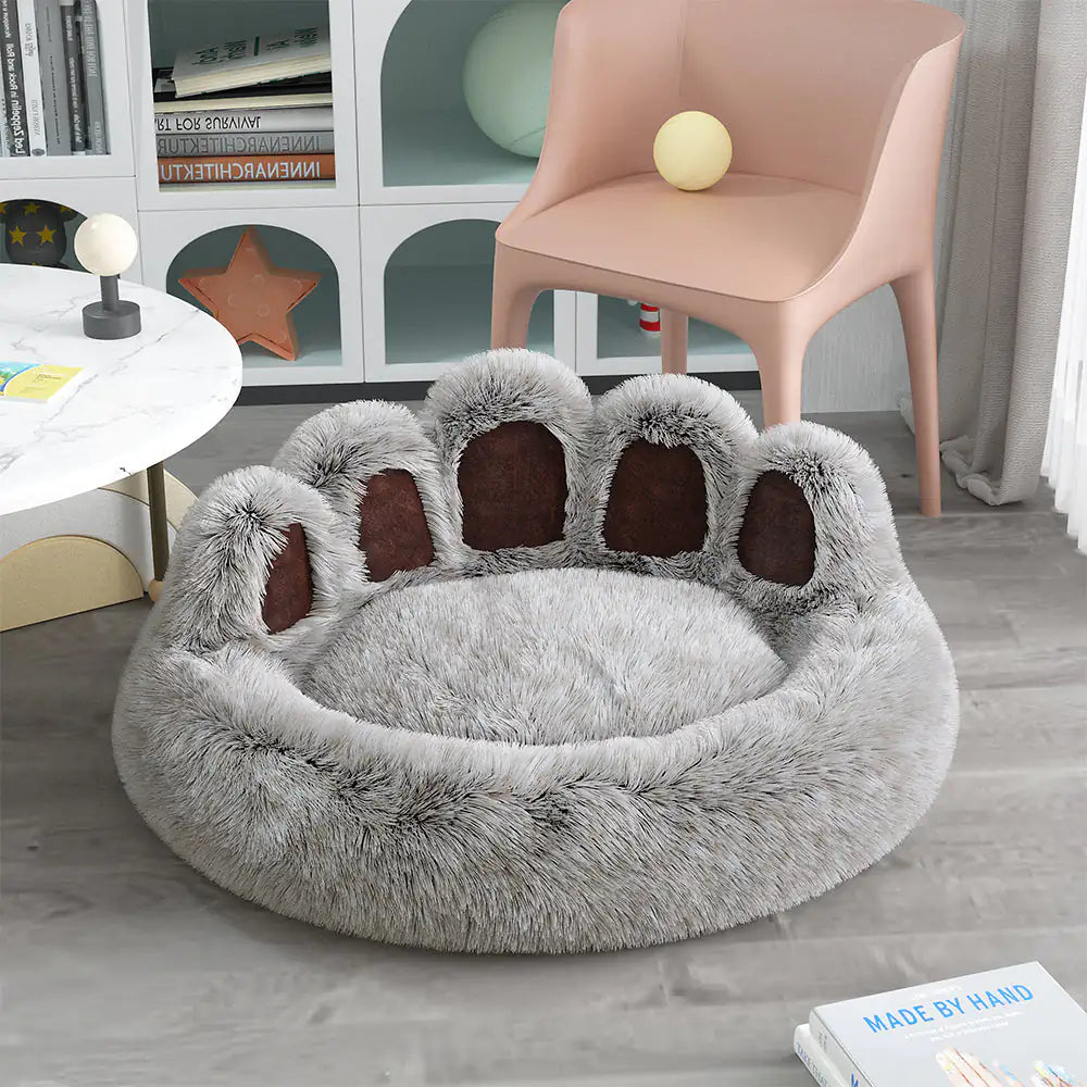 Fluffy paw-shaped pet bed in a room with a chair and books.